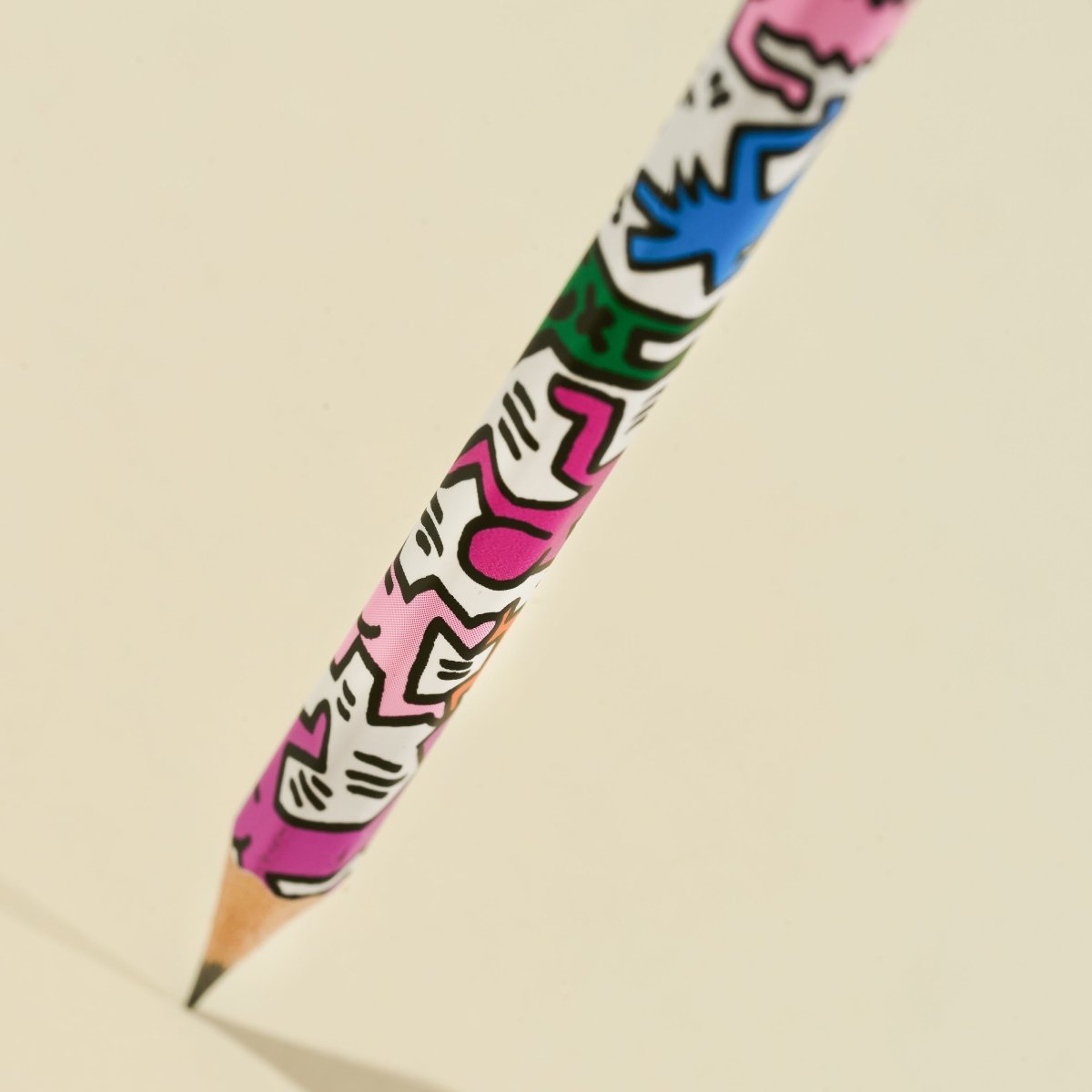 Angled close-up of the pencil point with Haring’s artwork in pink and green tones.