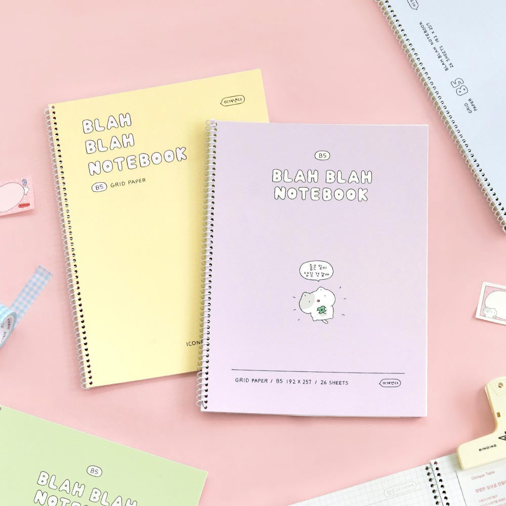 Iconic Blah Blah Spiral Grid Notebooks in cream yellow and lavender displayed on pink background with stationery.