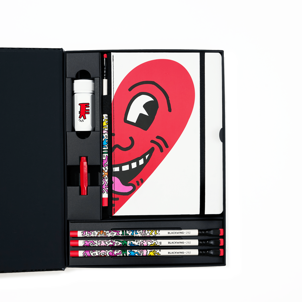 Open Blackwing Keith Haring gift set showing four pencils, sharpener, eraser, and “Smiling Heart” sketchbook in a black presentation box.