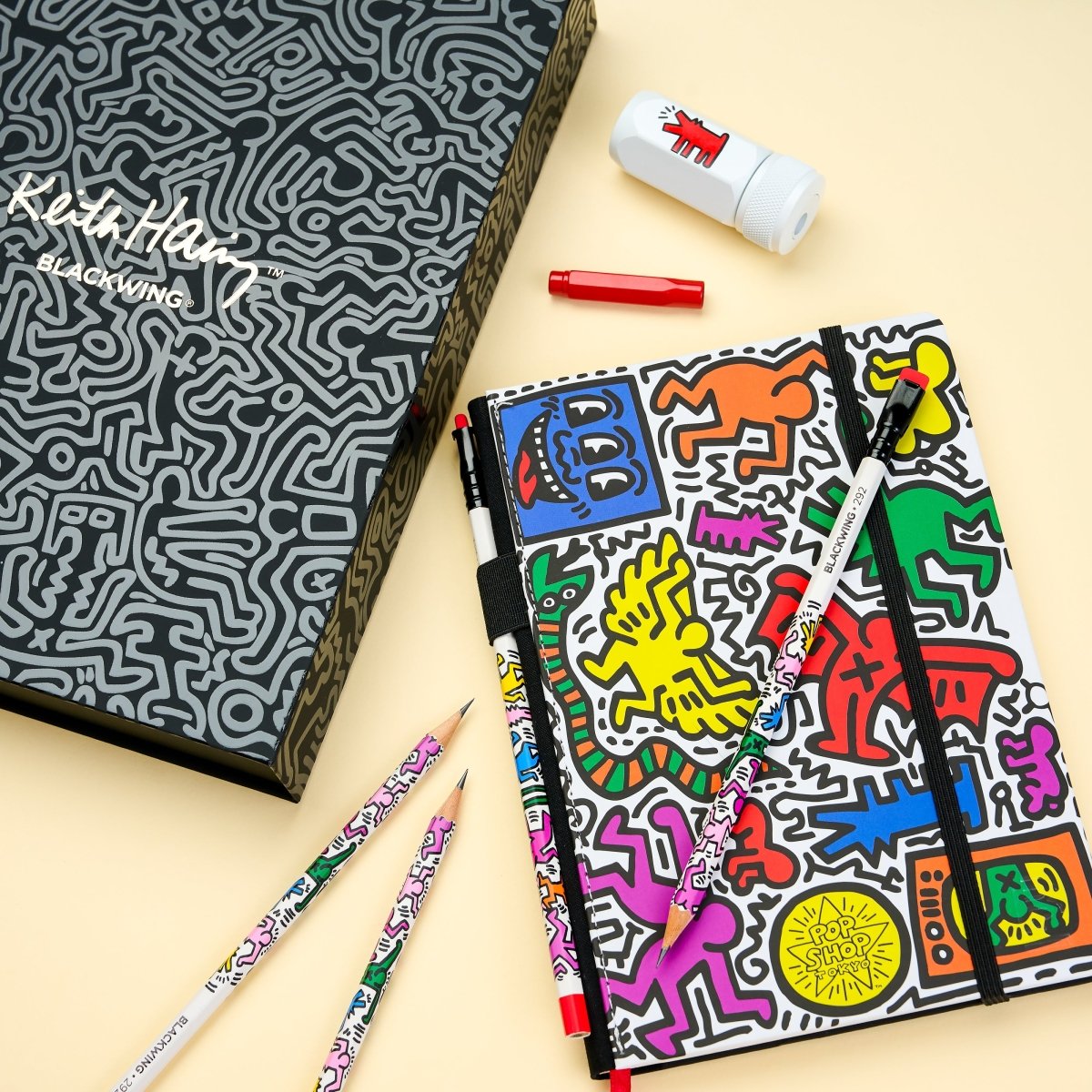 Gift set contents laid out, including sketchbook, pencils, sharpener, and eraser, with a second monochrome sketchbook in the background.