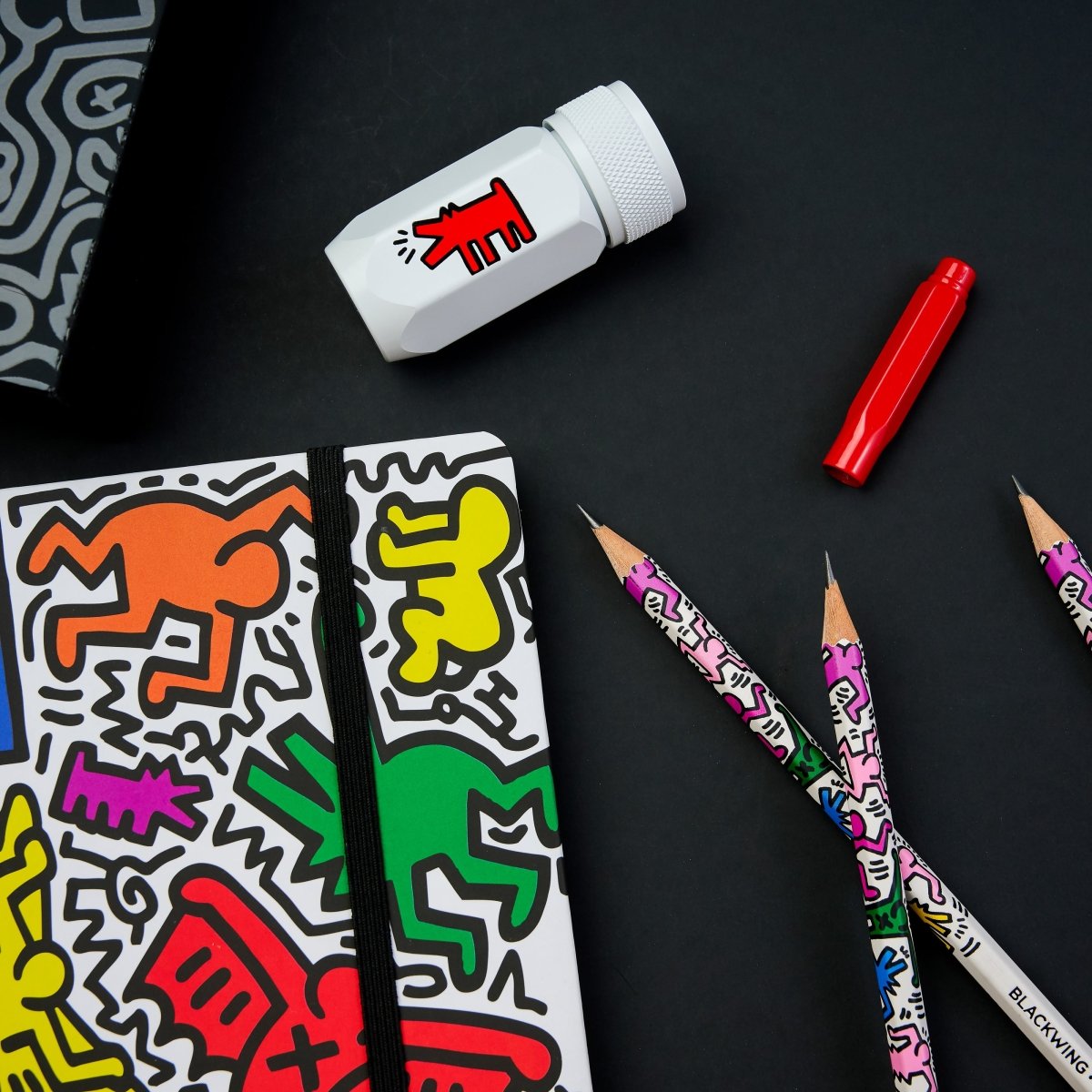 Selection of gift set items including vibrant sketchbook, eraser, and two Blackwing pencils with Haring-inspired designs.
