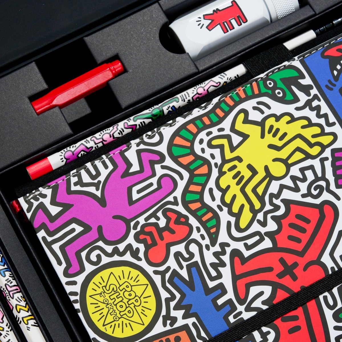 Detail view of the open box showing sharpener and sketchbook with colourful Haring illustrations.
