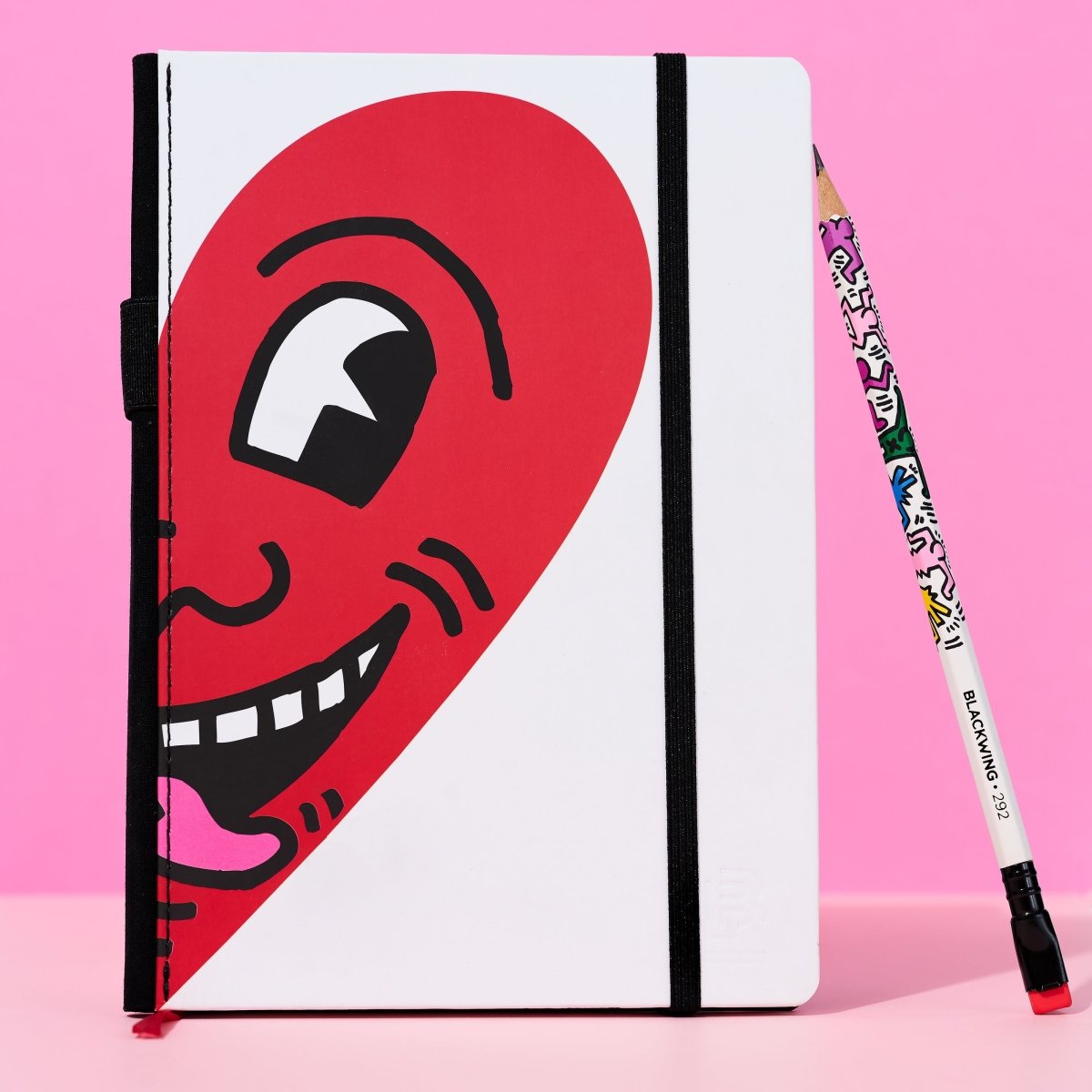 Close-up of the notebook and Blackwing pencil with a pink background, showing Haring’s artwork in detail.