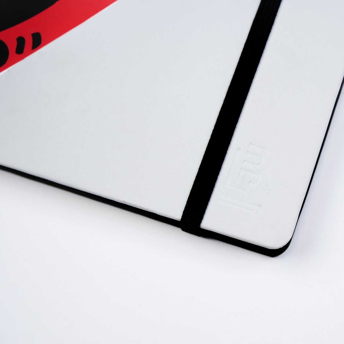 Detail view of the notebook’s black spine and elastic closure against the white cover.