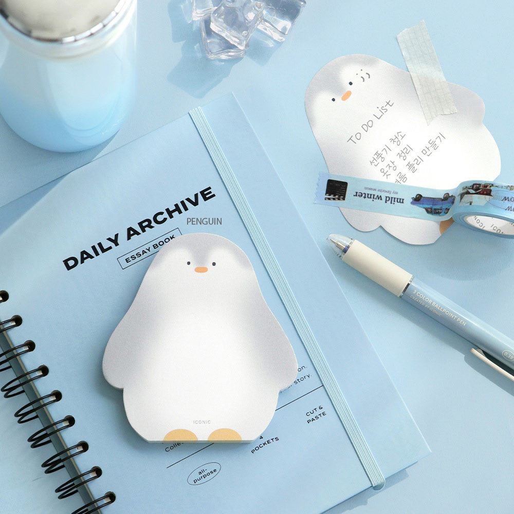A penguin-shaped Iconic Animal Memo Pad opened on a light blue desk with stationery and a close notebook.