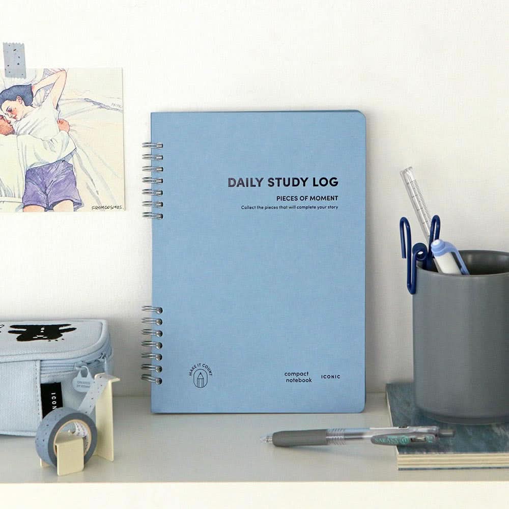 Blue Iconic Daily A5 Study Planner standing upright on a desk beside stationery and a photo, showcasing its clean and minimal design.
