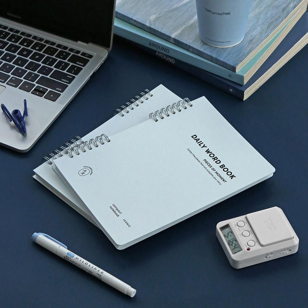 Iconic Daily A5 Word Vocabulary Notebook in blue cover shown with pen and laptop.