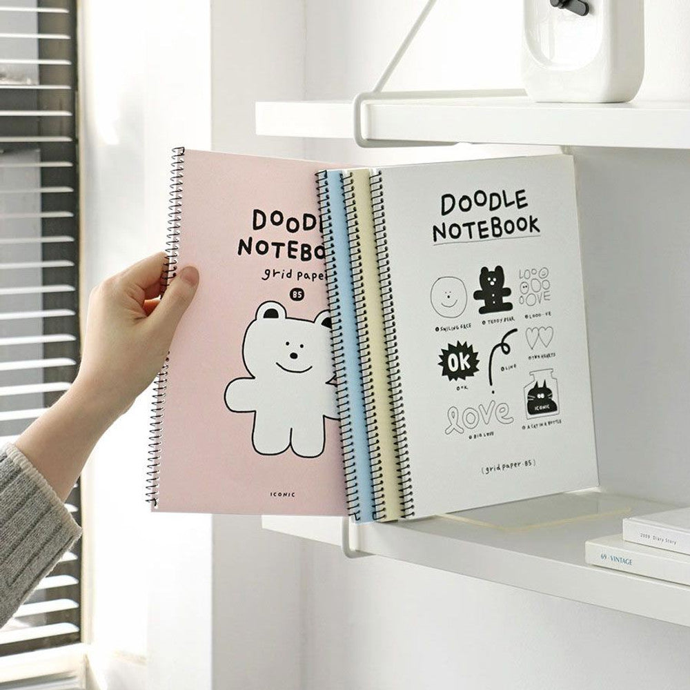 Iconic Doodle B5 Grid Notebook with pink bear cover being placed on white shelf.