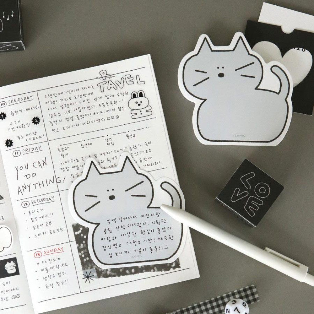 Grey cat-shaped Iconic Doodle Cat Memo Pad used as a tear-off note inside an open planner with pen and stationery on desk.