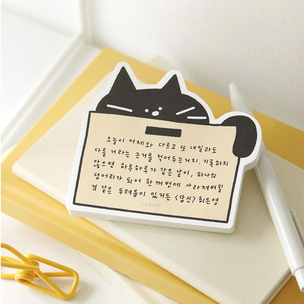 Black cat-shaped Iconic Doodle Cat Memo Pad “Box” design with beige note space placed on stacked notebooks with pen and paperclip.