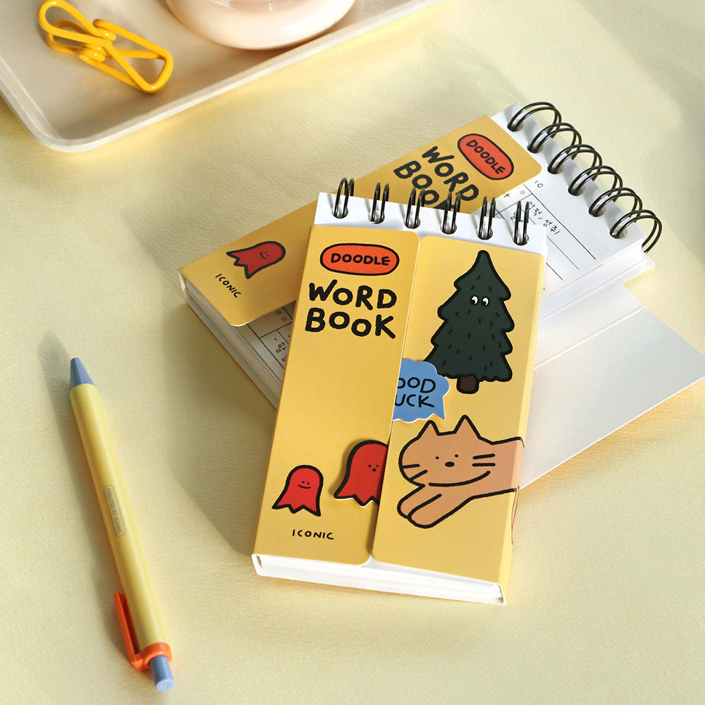 A yellow Iconic Doodle Word Compact Size Notebook placed beside pencils and paper clips on a light desk.