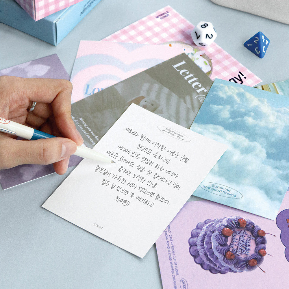 Person writing on Iconic Moodscape Message Card with blue envelope and stationery beside.