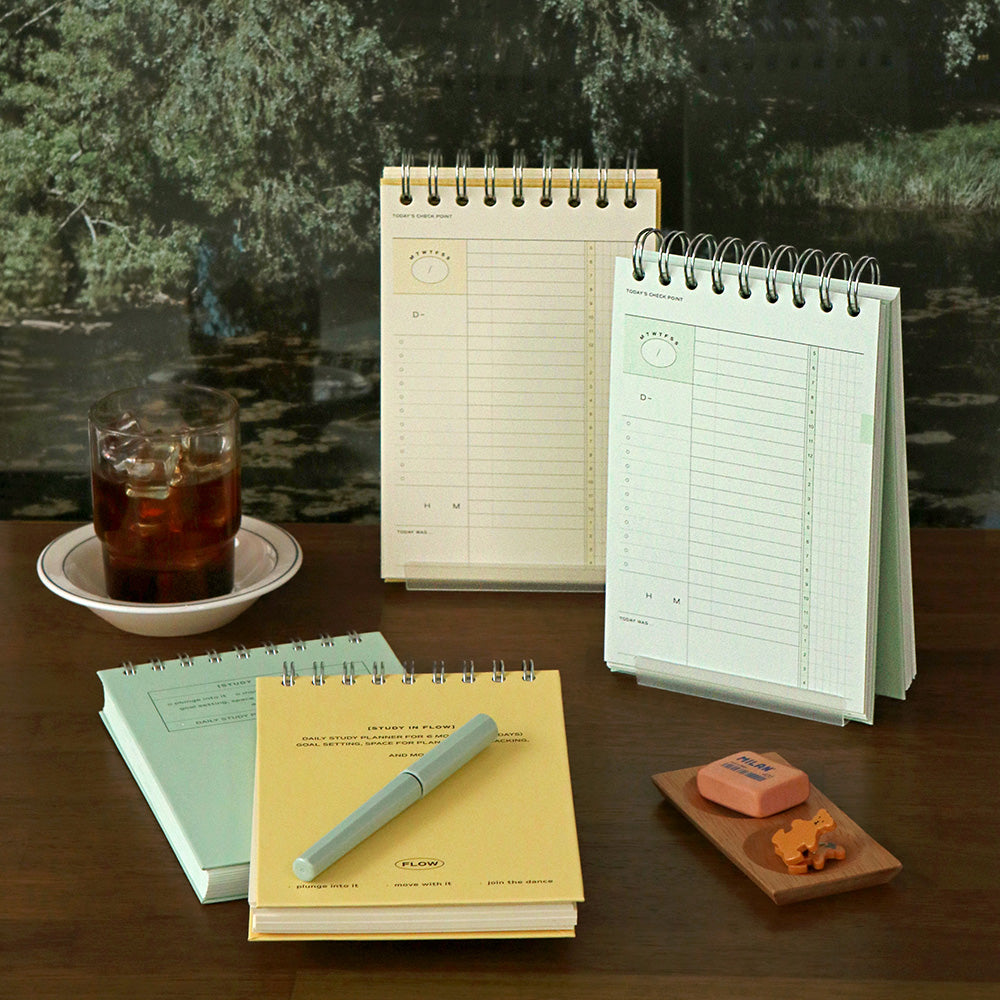 Iconic Undated Flow Spiral Study Planners in butter yellow and vintage green covers displayed together with pens and books.