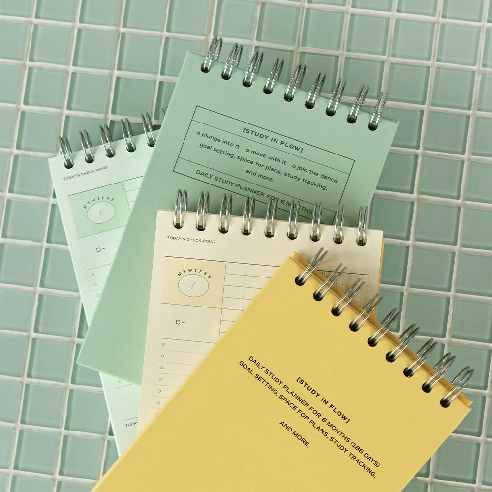 Iconic Undated Flow Spiral Study Planners in butter yellow and vintage green shown on tiled background with study accessories.