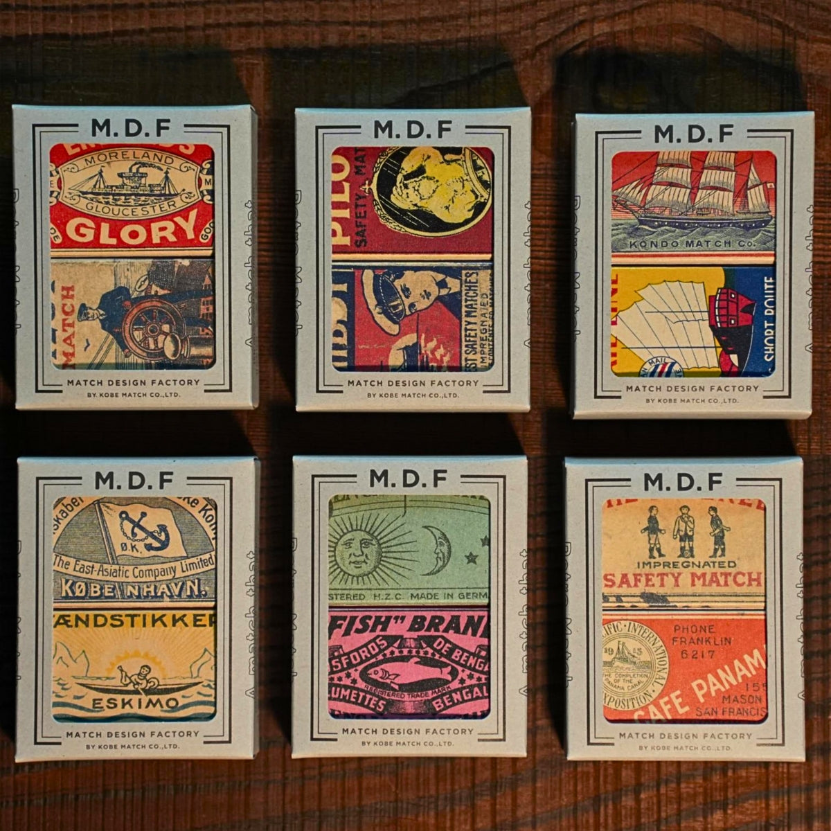 Six vintage-style matchboxes with colorful designs on a wooden surface